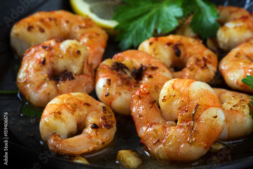 фотографія prawns shrimps roasted in a black pan with garlic, lemon and italian parsley gar