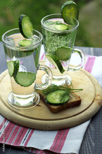 Cold drinking water in a glass with a cucumber on a wooden board