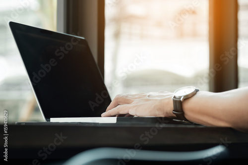 Attractive man in casual business sitting at a table working on his laptop computer at home office in front of a window