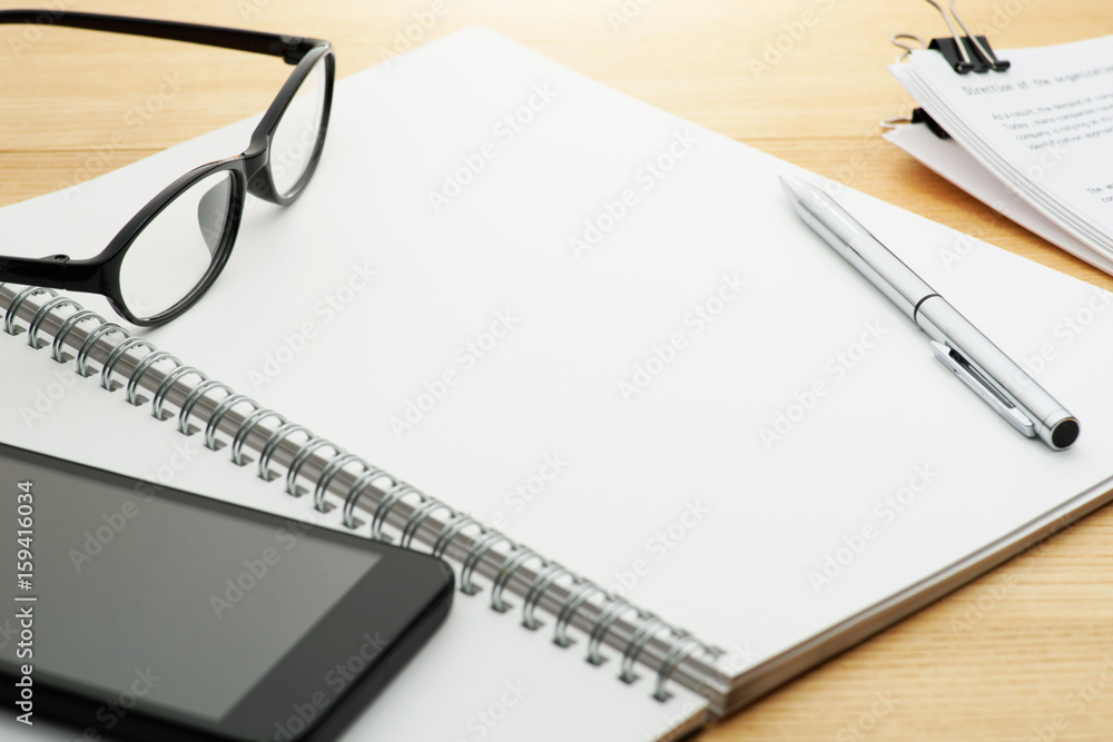 Open notebook on bright wood table. Pen, notebook, smartphone, glasses and documents on wooden desk.
Open notebook on bright wood table. Pen, notebook, smartphone, glasses and documents on wooden desk.