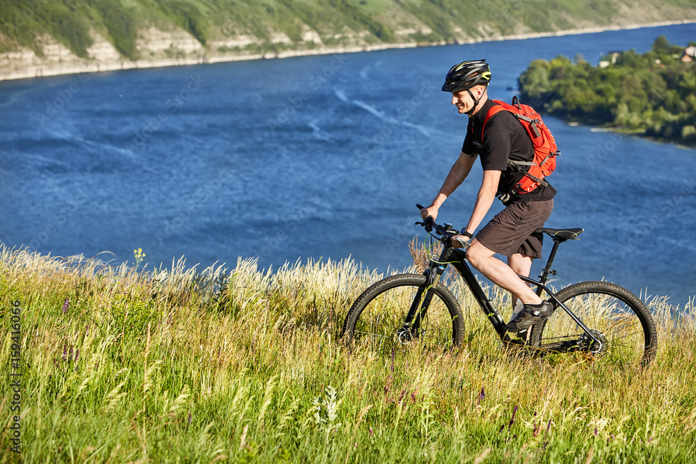 Attractive cyclist riding the mountain bicyclist on the summer trail above the river. Attractive cyclist riding the mountain bicyclist on the summer trail above the river.
