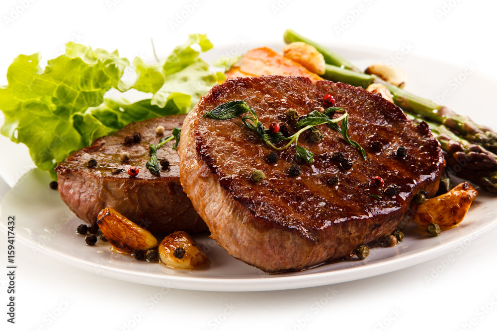 Grilled beef steaks with asparagus and carrots on white background 