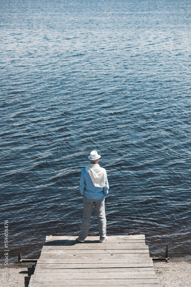 back view of casual man standing on quay in front of water surface at daytime