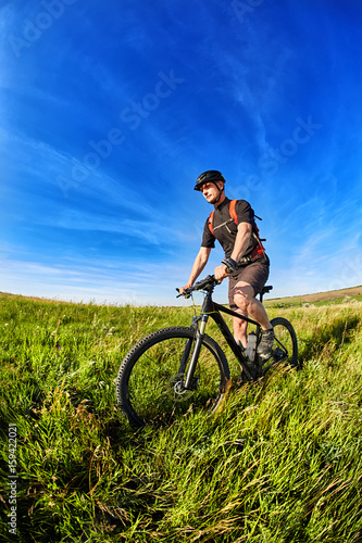 Young cyclist riding mountain bicycle through green meadow against beautiful sky.