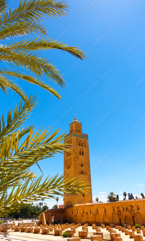 Historic Koutoubia Mosque, Marrakech, Morocco, with sunlit palm tree leaves in the foreground.
