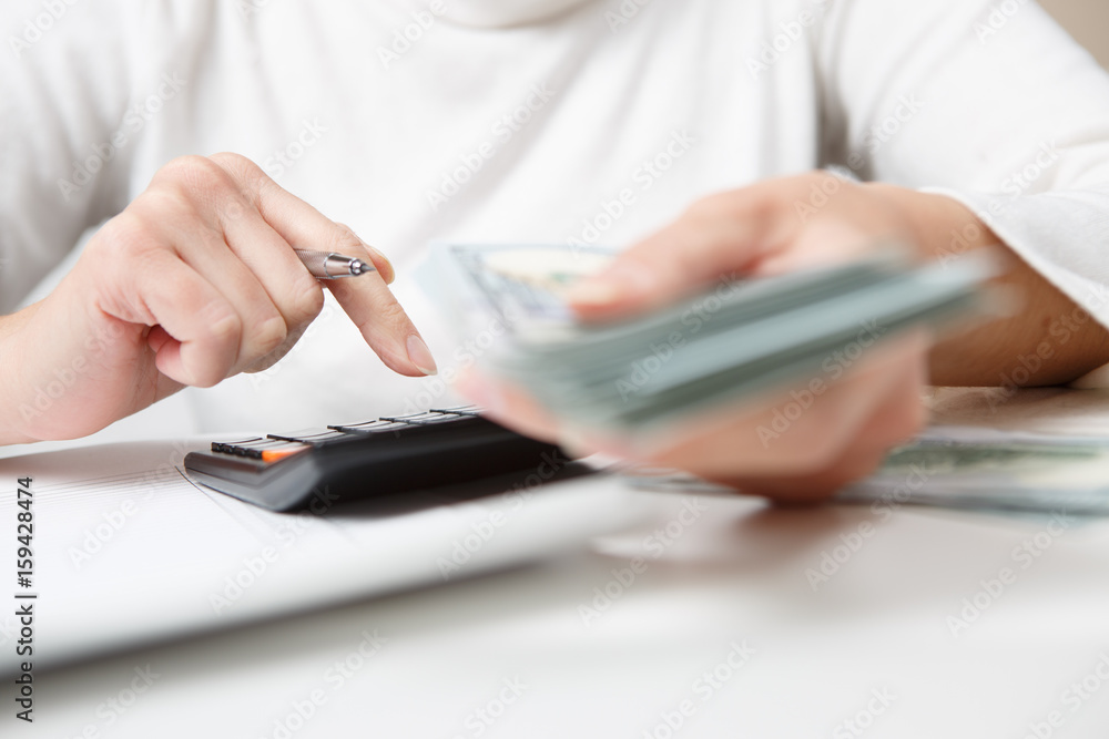 Fototapeta premium savings, finances, economy and home concept - close up of hands with calculator counting money and making notes at home