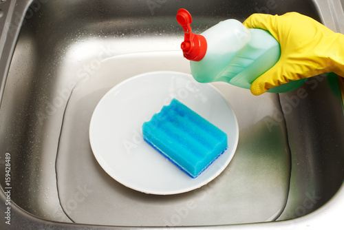 Kitchen sink with water, plate, blue cleaning sponge, detergent