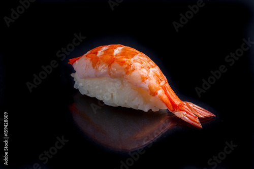 Shrimp sushi on a black glossy background.