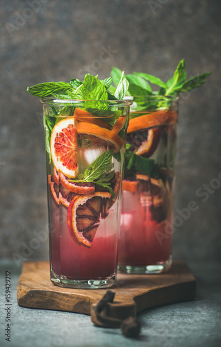 Blood orange citrus lemonade with mint and ice in tall glasses, dark brown stone background. Refreshing summer drink concept