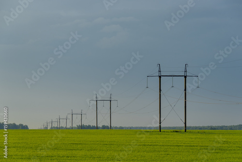 High voltage lines and power pylons in a flat and green agricultural landscape on at dawn