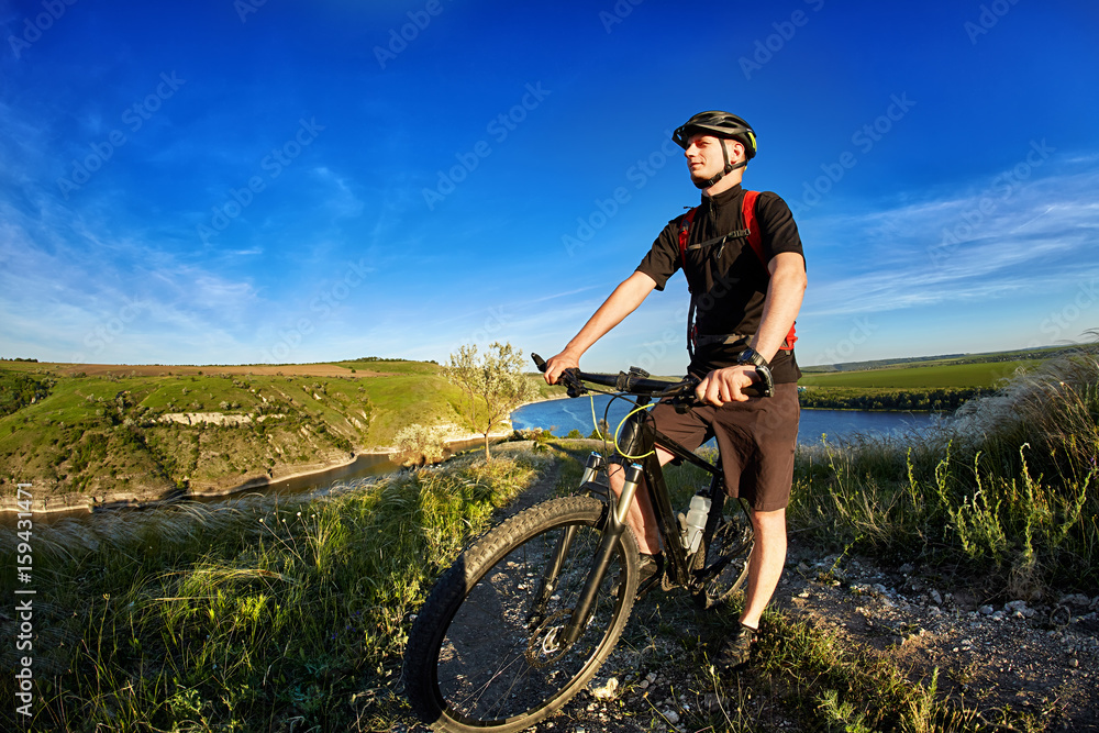 Portrait of the cyclist with mountain bike on a background of blue sky with clouds.