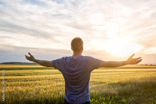 Man standing in an open field at sunset with open arms - embracing nature