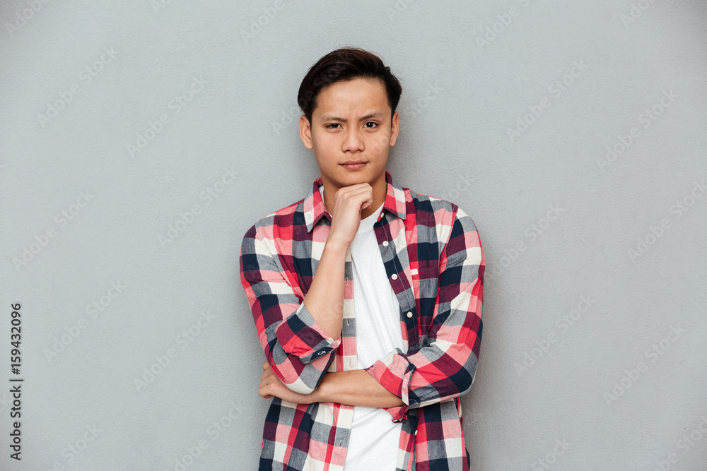 Fototapeta premium Serious asian man standing over grey wall.