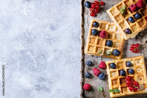 Homemade square belgian waffles with fresh ripe berries blueberry, raspberry, red currant on vintage metal tray over gray texture background. Top view with space