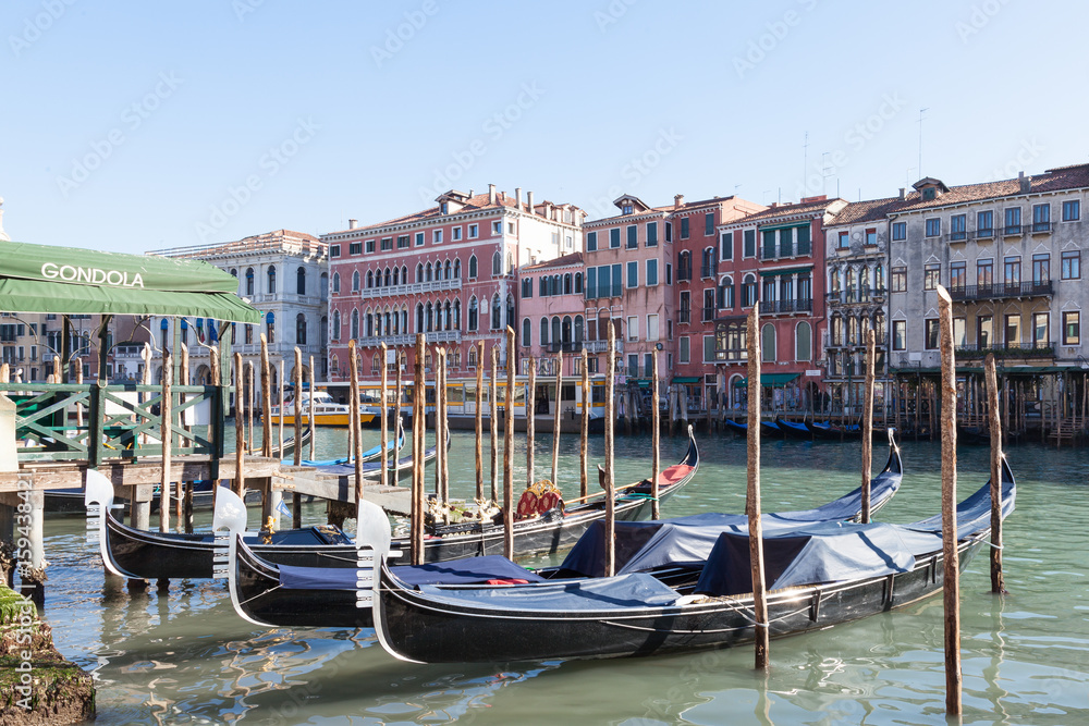 Row of gondolas moored on the Grand Canal , Venice , Italy  in front of ancient palazzos in San Polo with the gondola station alongside in a tourism and travel concept