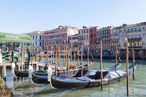 Row of gondolas moored on the Grand Canal , Venice , Italy  in front of ancient palazzos in San Polo with the gondola station alongside in a tourism and travel concept photo