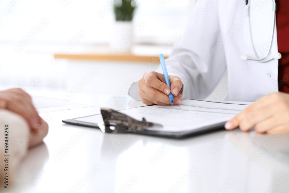 Close up of a female doctor filling up an application form while consulting patient Close up of a female doctor filling up an application form while consulting patient