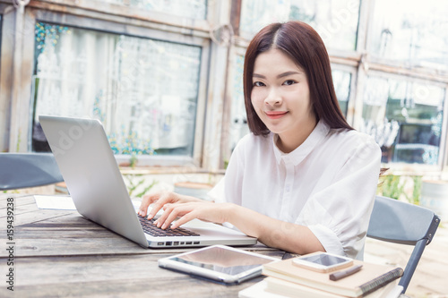 young happy asian woman using technology on her laptop computer and looking at camera