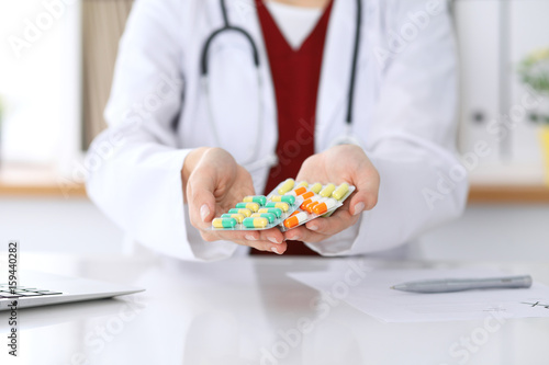 Female doctor hand holding pack of different tablet blisters at workplace closeup