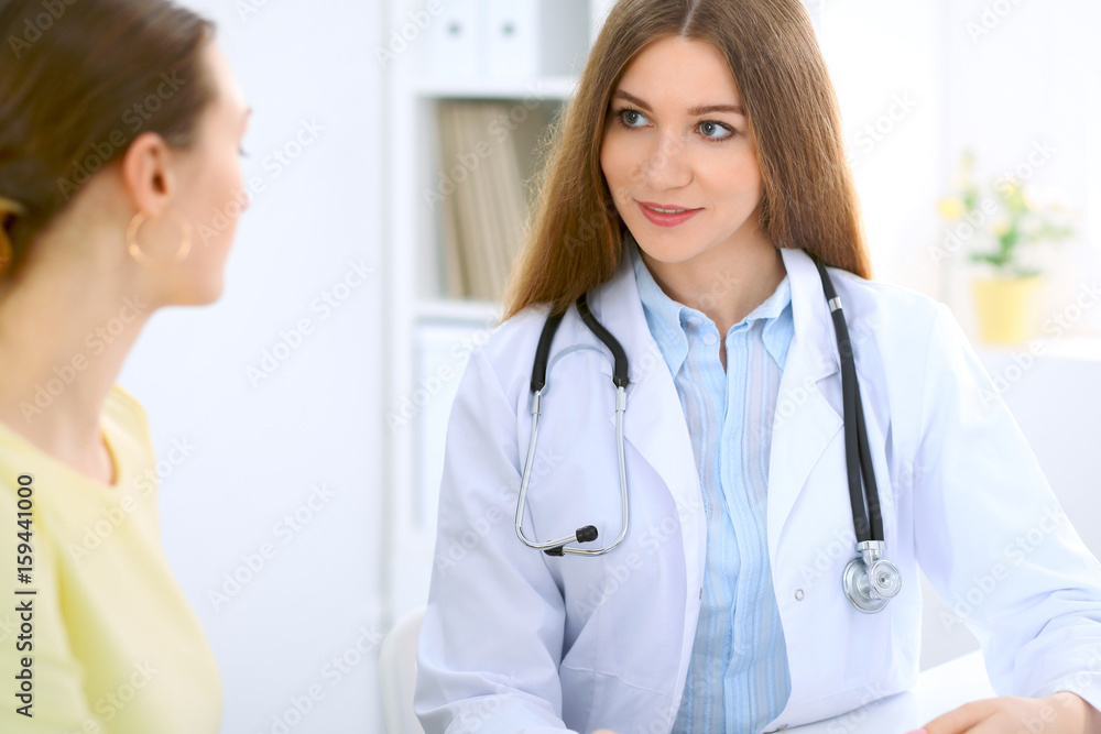 Doctor and patient have a talk while sitting at the desk near window Doctor and patient have a talk while sitting at the desk near window