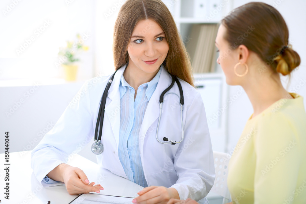 Doctor and patient have a talk while sitting at the desk near window Doctor and patient have a talk while sitting at the desk near window