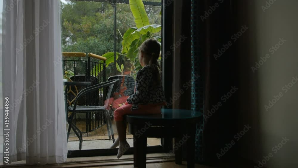 little girl sitting and watching on the backyard from the inside. Wants to play but its heavy rain outside little girl sitting and watching on the backyard from the inside. Wants to play but its heavy rain outside