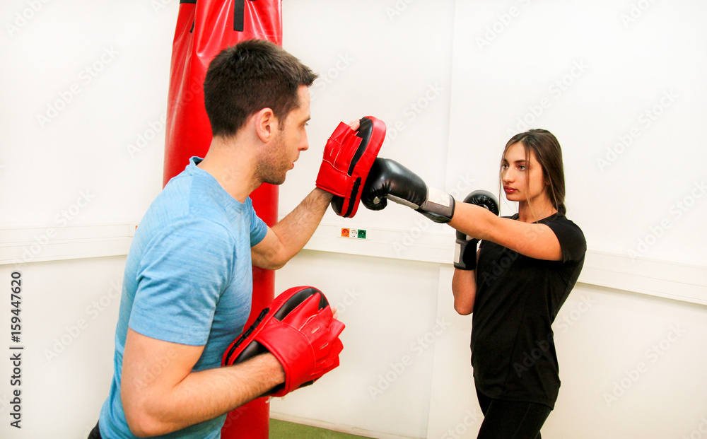 The female boxer training at gym. Young sporty woman punching her male partner with red boxing gloves at gym club. Attractive sports girl is practicing with a handsome trainer in the sport center.