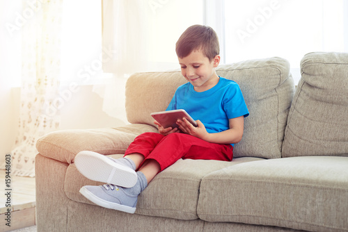 Side view of small boy sitting on sofa with tablet