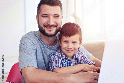 Close-up of small boy sitting with father at the table and using laptop