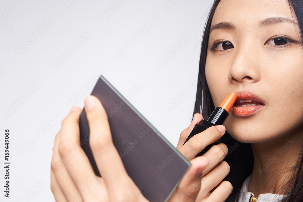 Woman paints lips, woman with mirror on light background Woman paints lips, woman with mirror on light background