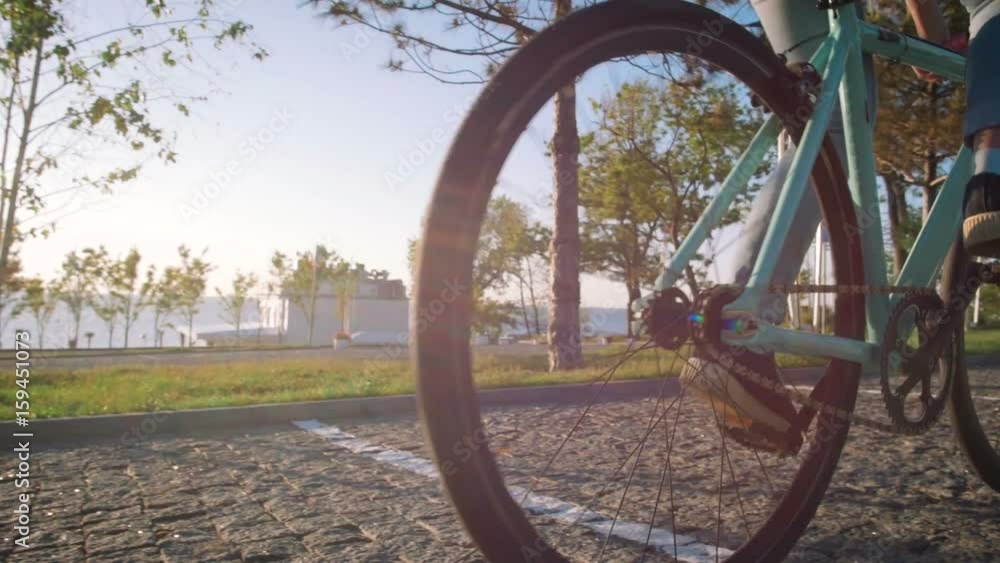 Young stylish woman cyclist enjoying fixed gear bike riding outdoors at sunrise near the sea, close up