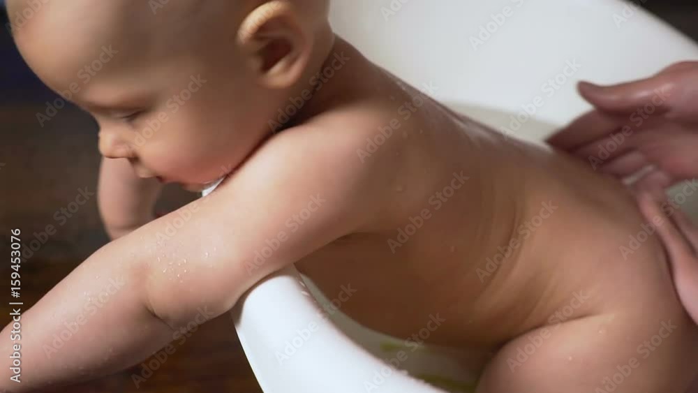 Newborn baby is covered with water drops closeup playing and smiling in the bath Newborn baby is covered with water drops closeup playing and smiling in the bath