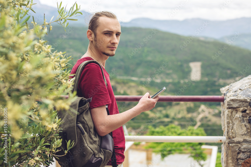 Man traveler with backpack looking at his smartphone on the background of nature and the mountains Man traveler with backpack looking at his smartphone on the background of nature and the mountains