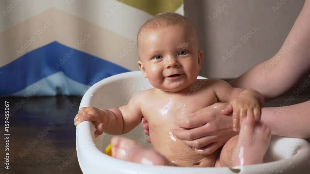 Newborn baby is covered with water drops closeup playing and smiling in the bath Newborn baby is covered with water drops closeup playing and smiling in the bath