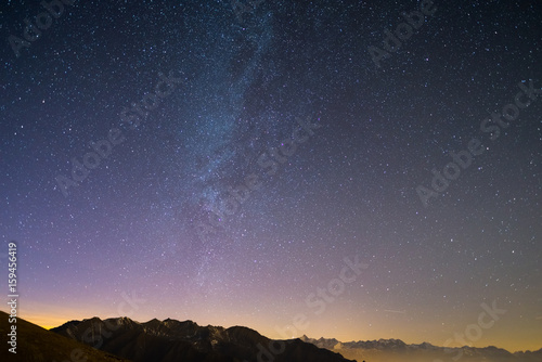 The wonderful starry sky on Christmas time and the majestic high mountain range of the Italian French Alps, with glowing villages below and moonlight.