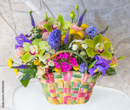 Colored basket filled with soft fresh flowers from the fields, meadows and gardens. basket is on the table against the background of a stone wall.