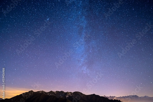 The wonderful starry sky on Christmas time and the majestic high mountain range of the Italian French Alps, with glowing villages below and moonlight.