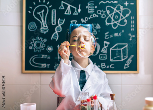Little boy scientist playing with soap bubbles against of drawn blackboard