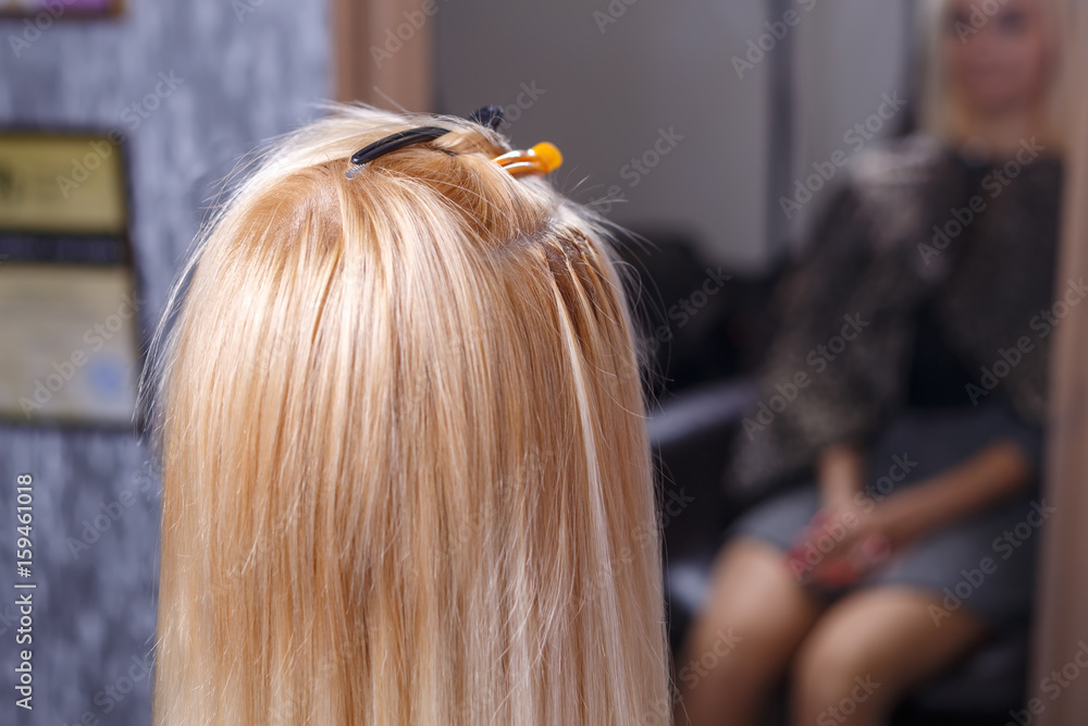 Hair extensions procedure. Hairdresser does hair extensions to young girl, blonde in a beauty salon. Selective focus. Hair extensions procedure. Hairdresser does hair extensions to young girl, blonde in a beauty salon. Selective focus.