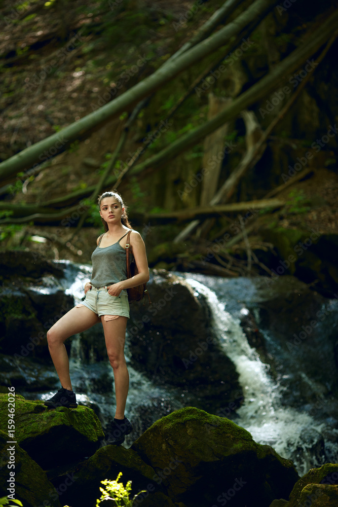 Hiking in forest with waterfall in background. Woman trekking in mountains against waterfall. Female with backpack on hike in nature. Cascading waterfall Hiking in forest with waterfall in background. Woman trekking in mountains against waterfall. Female with backpack on hike in nature. Cascading waterfall