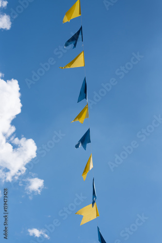 Fototapeta Naklejka Na Ścianę i Meble -  blue and yellow bunting flags on string waving in wind at funfair festival against blue summer sky