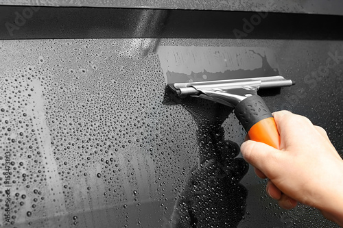 Worker with squeegee washing tinted car window