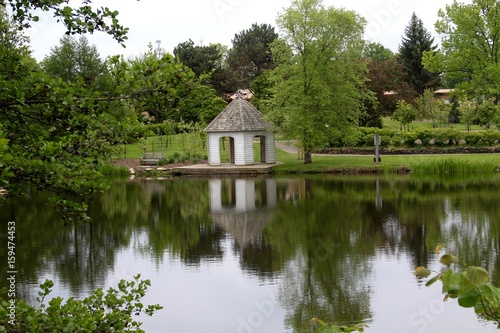 The white gazebo in the park reflecting of the water of the lake.