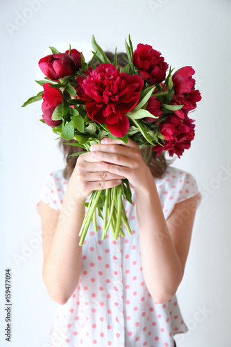 Young woman holding bunch of peonies on white background