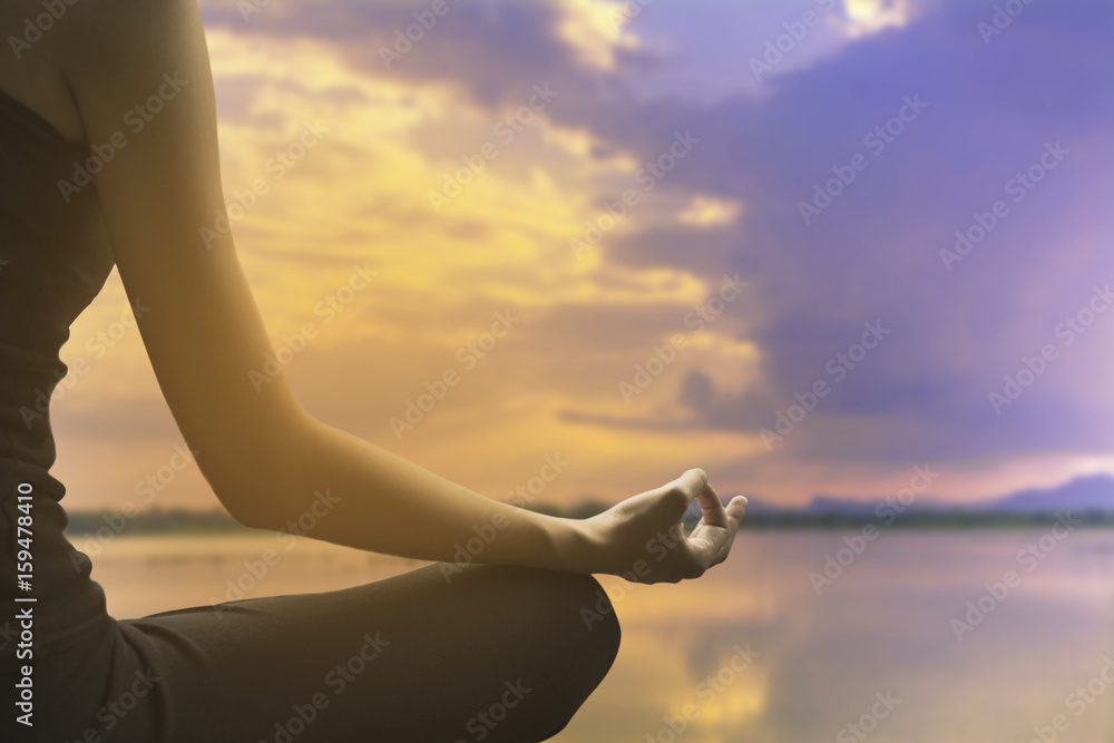 Close-up of feminine and masculine arms and crossed legs during meditation on river with sky background.