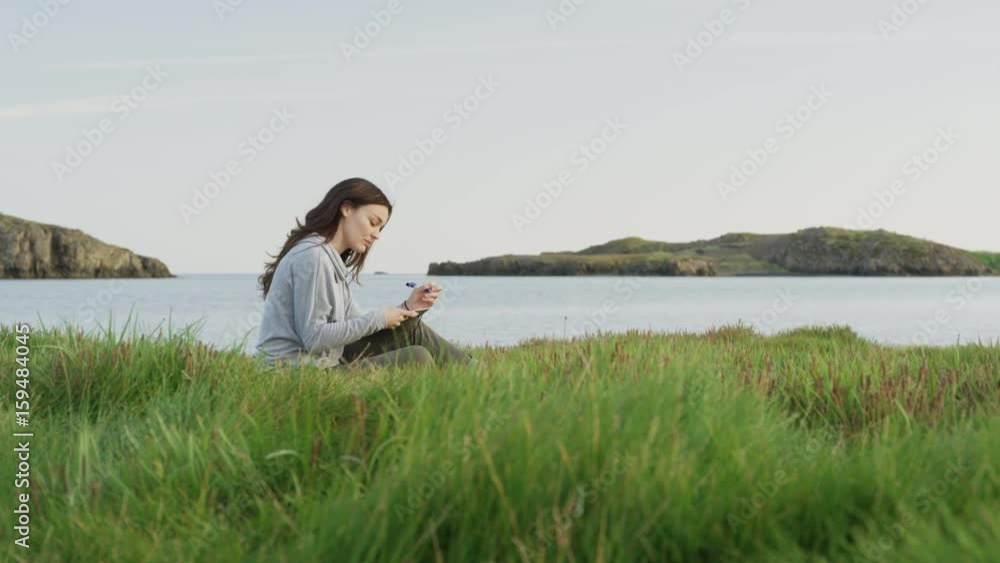 Wide panning shot of woman writing in journal near river. Borgarnes, Snaefellsnes, Iceland Wide panning shot of woman writing in journal near river. Borgarnes, Snaefellsnes, Iceland