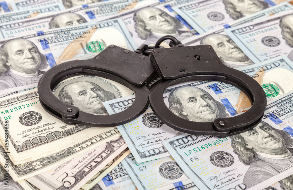 Steel police handcuffs lying on the background of american dollars Steel police handcuffs lying on the background of american dollars