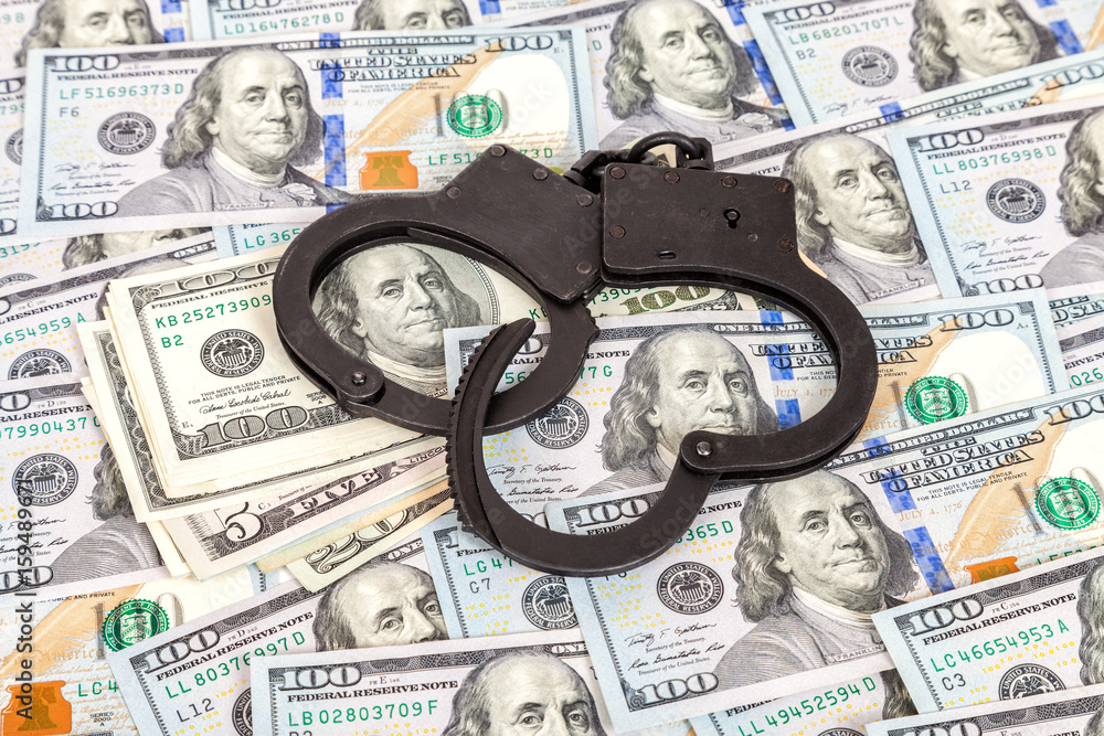 Steel police handcuffs lying on the background of american dollars Steel police handcuffs lying on the background of american dollars