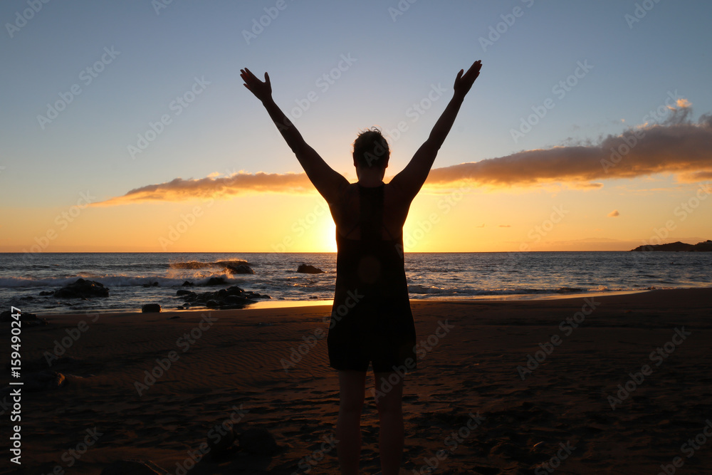 Frau am Strand im Sonnenuntergang streckt Hände in die Luft.