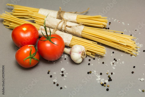 Italian ingredients of pasta and vegetables (tomatoes, pasta, garlic, pepper, cheese, spices) on a gray background. The concept of vegetarian food, health or cooking.